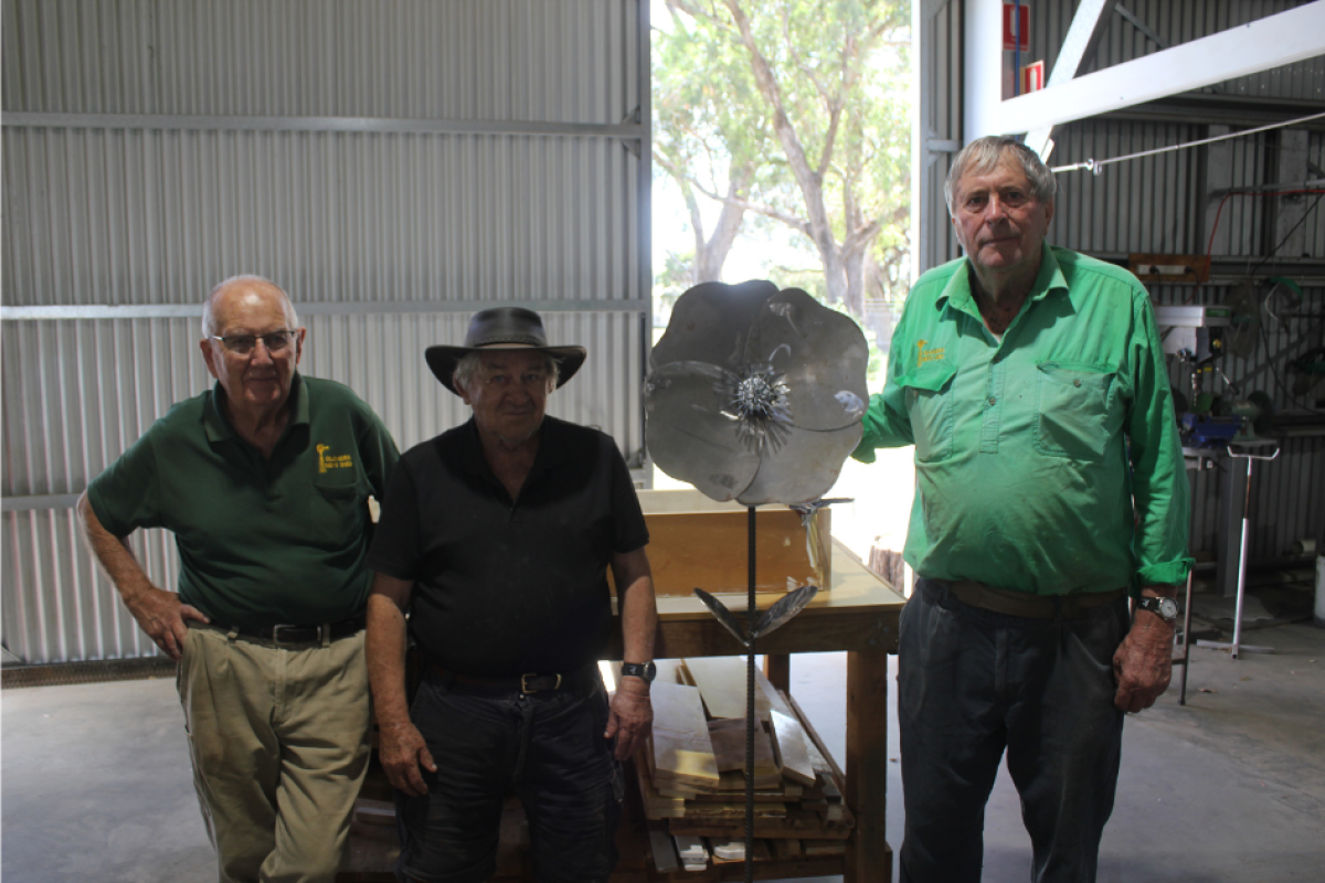 Bruce James, Ted Harland, and Phillip Yeo of the Gilgandra Men’s Shed stand with one of their popular recycled metal flowers, handmade by members of the shed. Photos by The Gilgandra Weekly: Nicholas Croker.